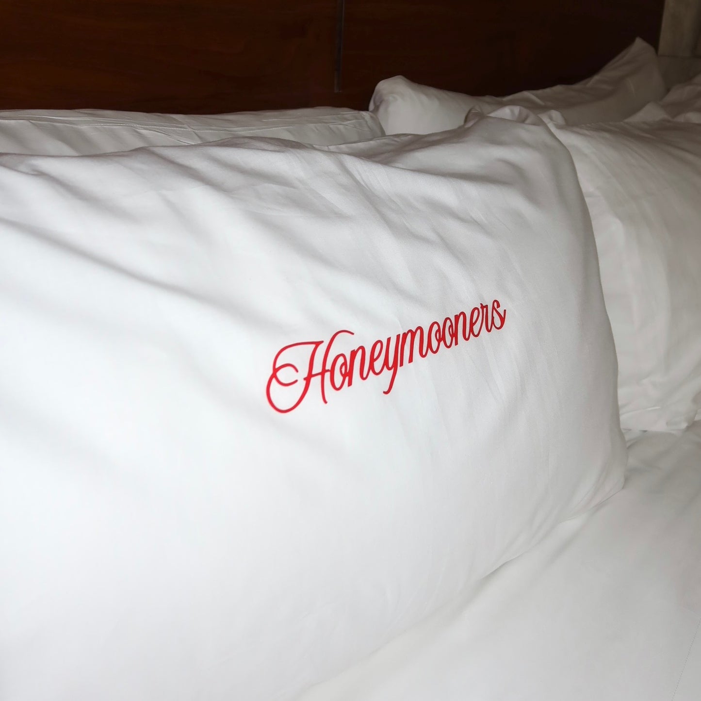 White pillow with 'Honeymooners' text in red on a bed.