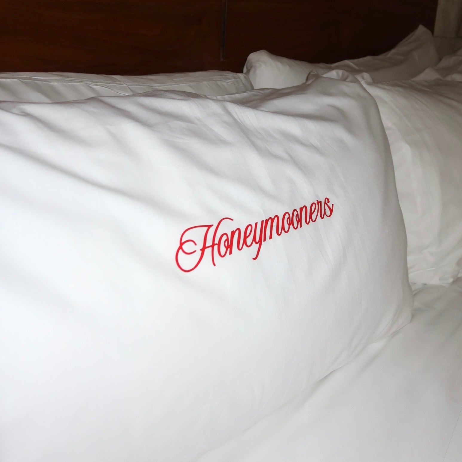 White pillow with 'Honeymooners' text in red on a bed.