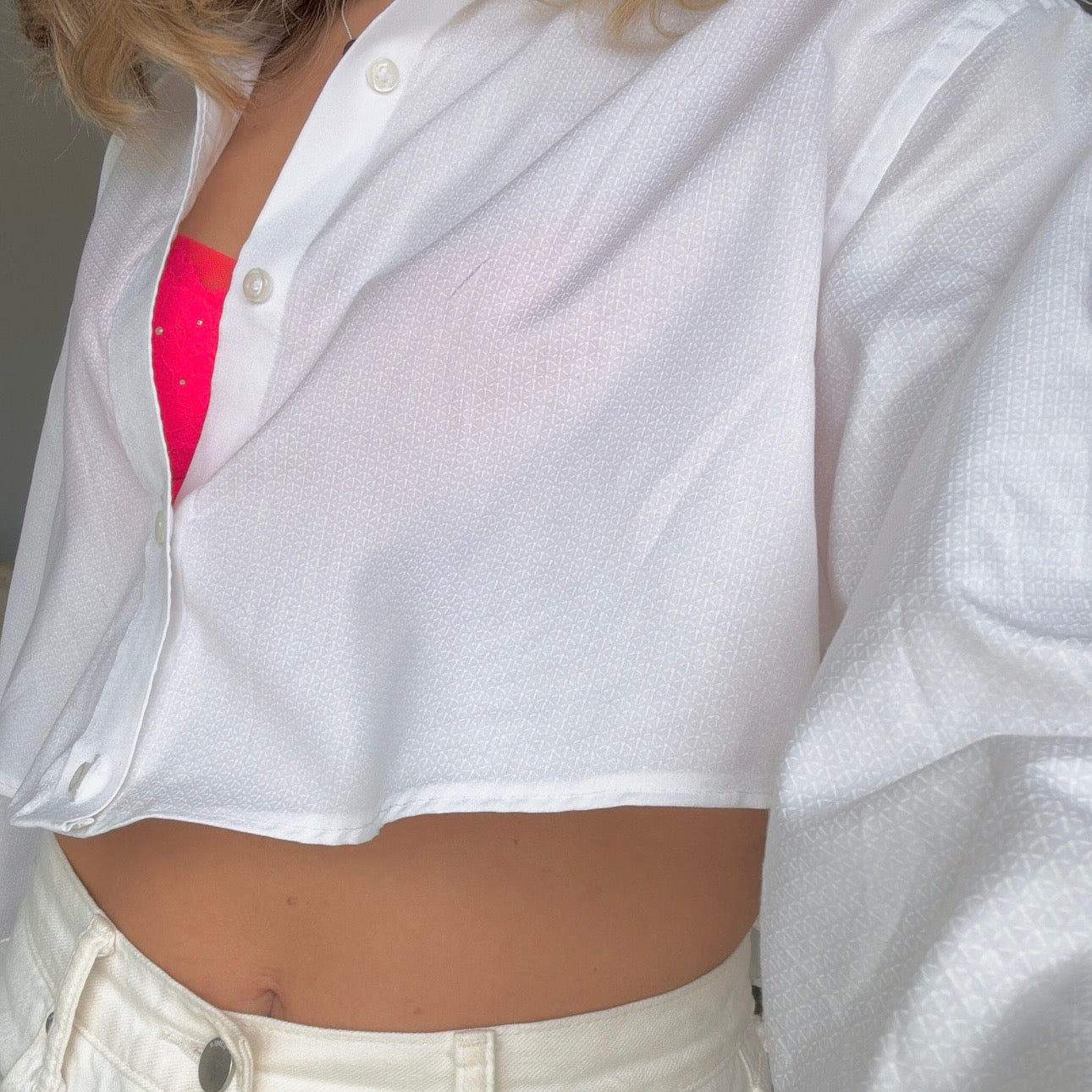 A close-up of a white button-up cropped shirt with a secret message written in red ink on the inside, worn over a pink bralette.