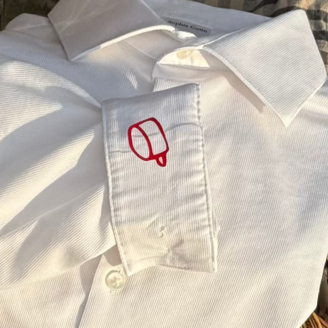 White shirt with a red logo on a table with tea set and coffee cup
