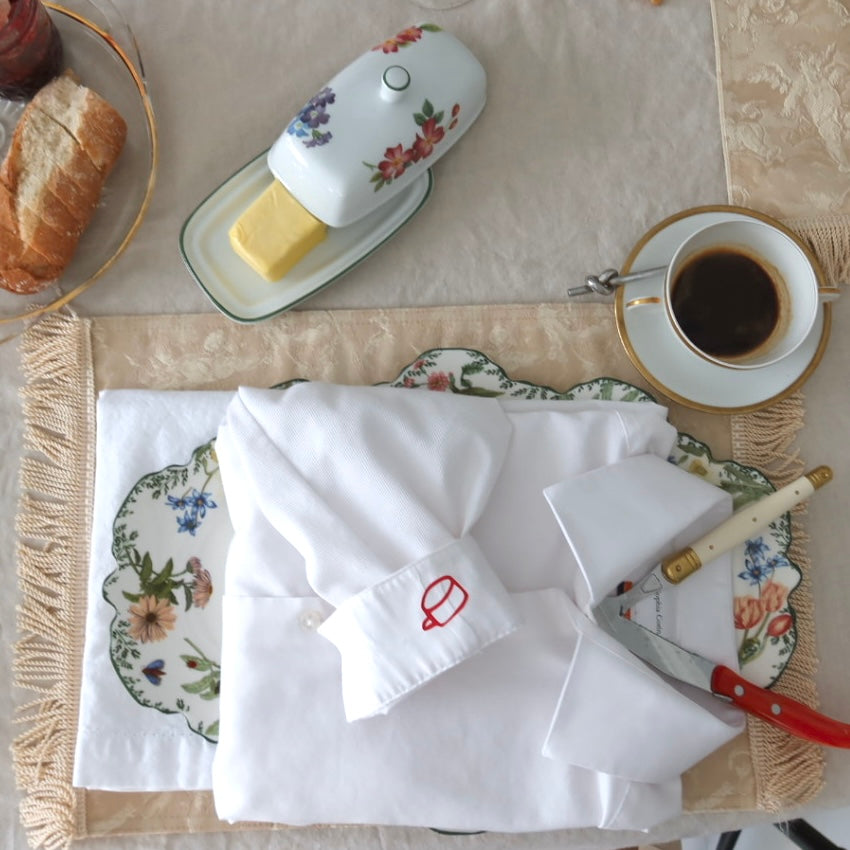 White apron with red logo on a table setting with coffee, bread, and butter.