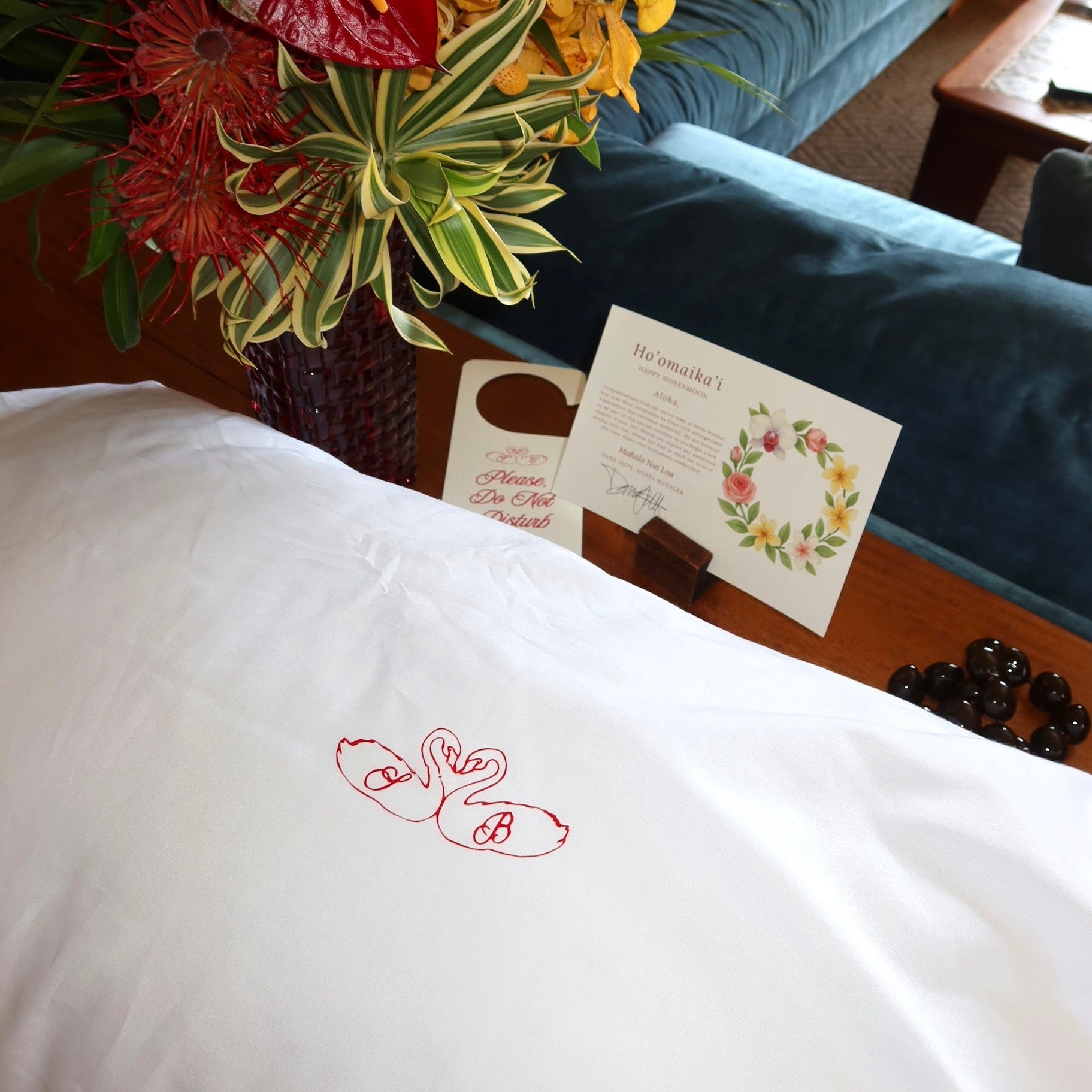 White pillow with red floral embroidery on a couch with flowers and a card in the background
