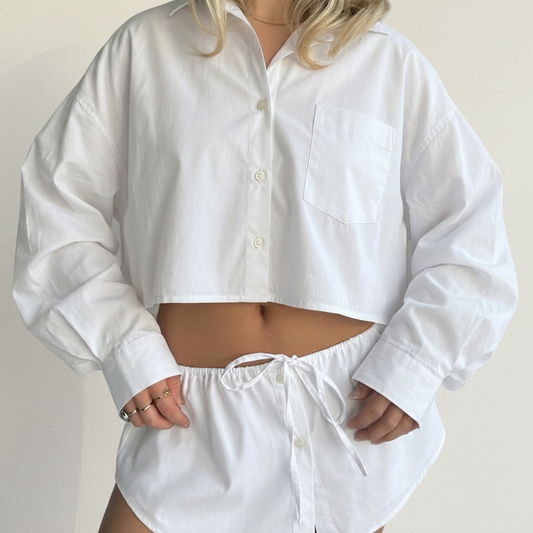 Person wearing a white button-up shirt and shorts on a plain background